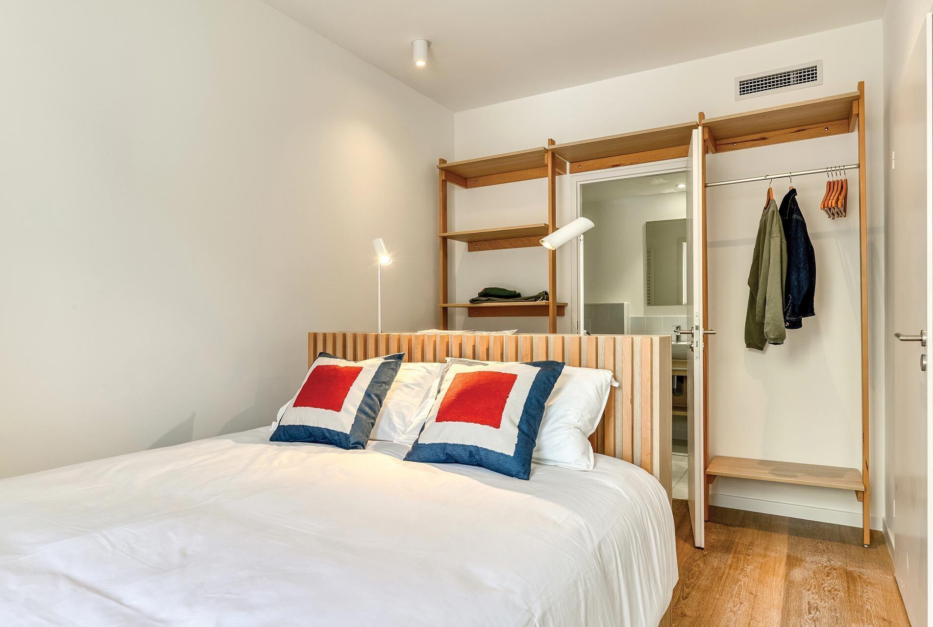 A bedroom with a bed, a wardrobe, a mirror, and a hanging coat rack.