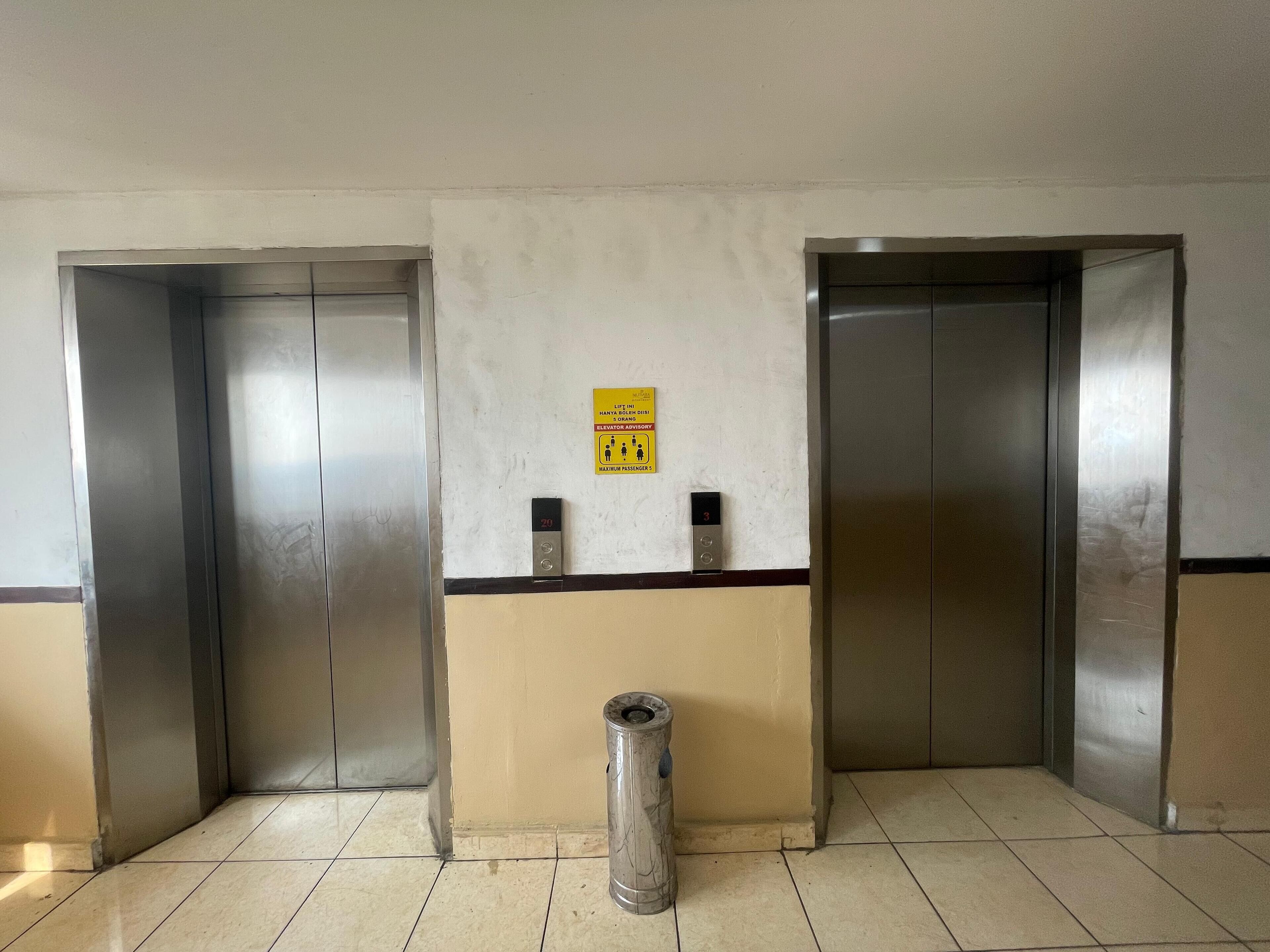 An elevator area with two closed elevator doors, a trash bin, and a sign indicating elevator access for the disabled.