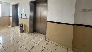 Un pasillo limpio y con baldosas, con un bote de basura, un interruptor de luz en la pared y una puerta que da a un ascensor.