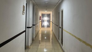 Un pasillo largo y estrecho con paredes blancas y suelo de baldosas, que conduce a un extremo luminoso.