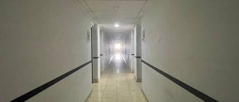 A long, narrow hallway with white walls and black trim, leading to a bright end.