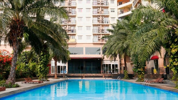 Una piscina rodeada de palmeras y un edificio de varios pisos con balcones.