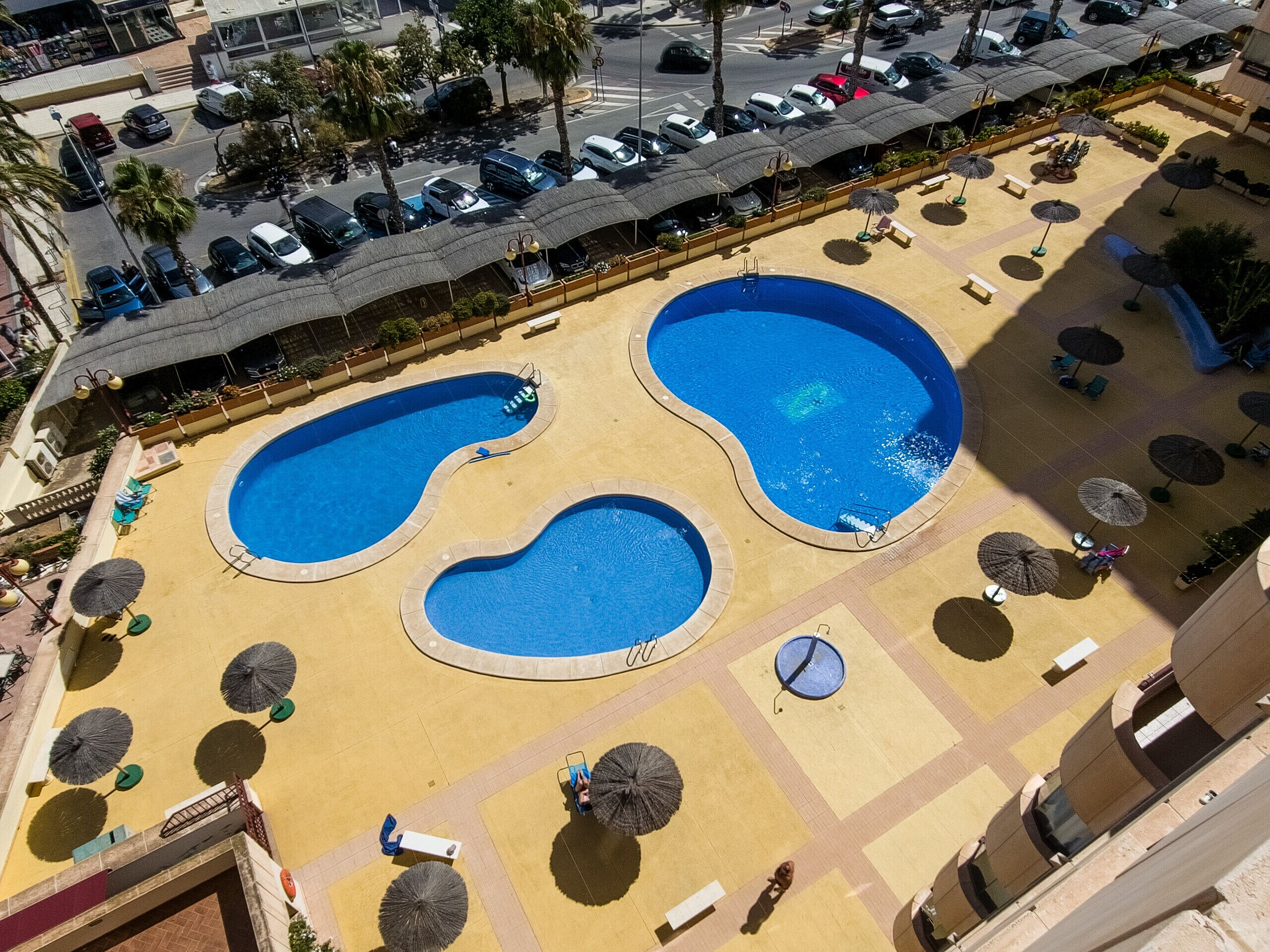 A rooftop pool area with two large pools, sun loungers, and umbrellas.