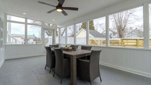 Un patio couvert avec une table et des chaises, de grandes fenêtres et un ventilateur de plafond.