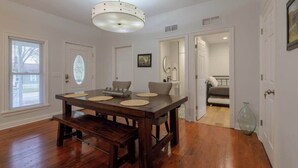 Un coin repas avec une table et un banc en bois, un lustre et une vue sur un salon comprenant un canapé et un vase.