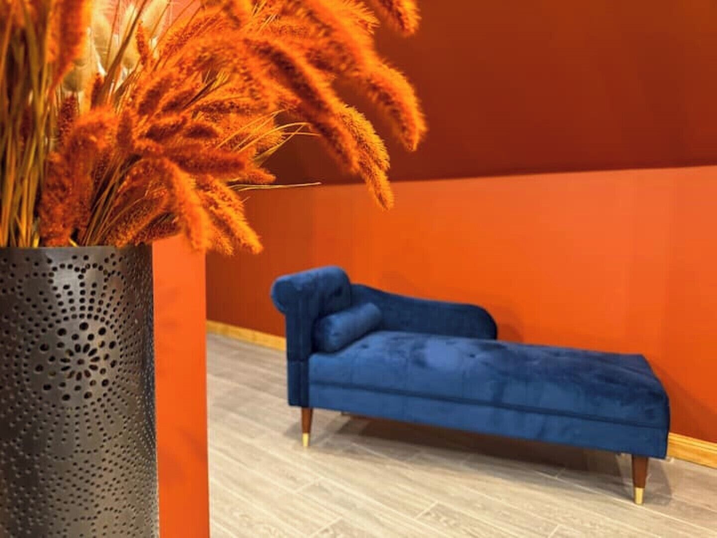 A room with a blue sofa, a decorative vase with orange flowers, and a wooden floor.