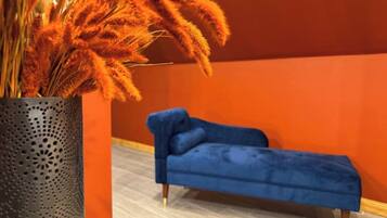 A room with a blue sofa, a decorative vase with orange flowers, and a wooden floor.