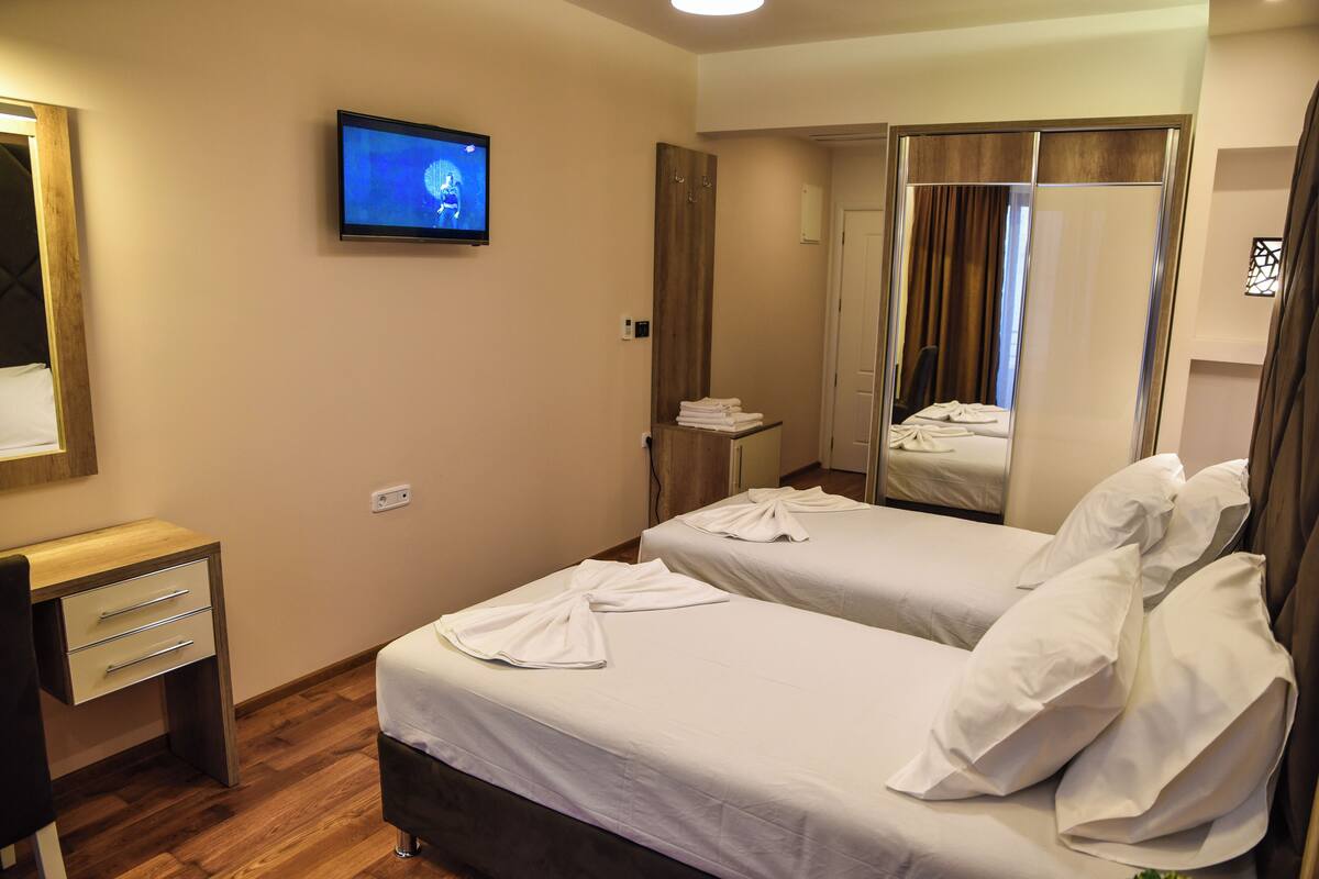 Una habitació d'hotel amb dos llits, un televisor penjat a la paret, una taula de treball i un mirall.