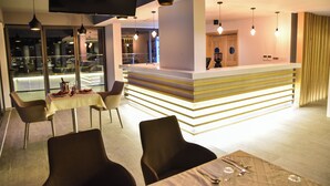 A modern restaurant with a counter, dining tables, and chairs. - Hotel Evropa (Ulcinj)