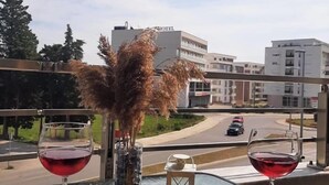 A table with two wine glasses, a fruit platter, and a vase with dried plants, overlooking a road and buildings. - Hotel Evropa (Ulcinj)