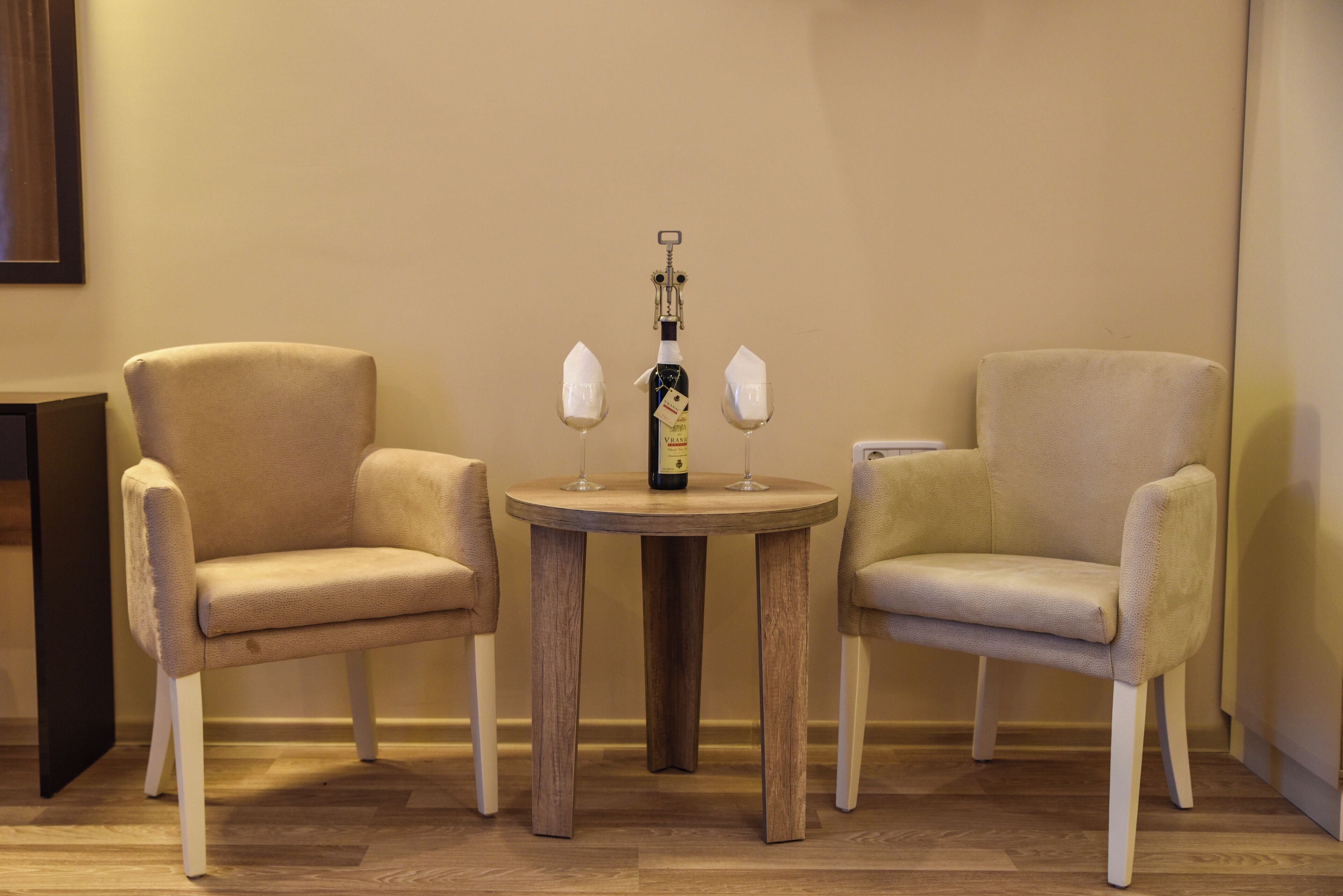 A small round wooden table with two beige armchairs and a bottle of wine.