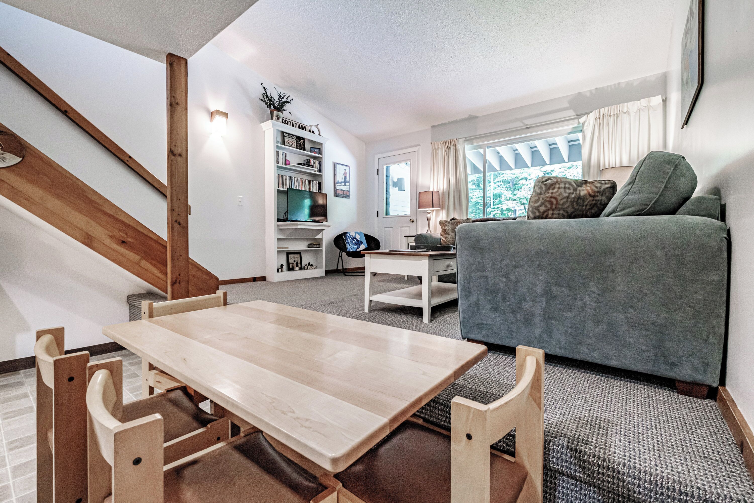 A cozy living room with a wooden dining table, a grey sofa, and a bookshelf.