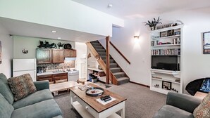 A modern living room with a sofa, coffee table, and a bookshelf. A staircase leads to the upper floor.
