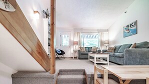 A cozy living room with a staircase, a sofa, a coffee table, and a dining table.