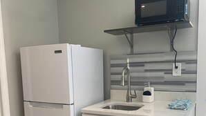 Une cuisine compacte avec un réfrigérateur blanc, un évier encastré et un four à micro-ondes placé au-dessus du plan de travail.