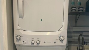 Un lave-linge à chargement frontal doté d’un panneau de commande, d’un évier et d’une étagère sur laquelle sont disposés des objets décoratifs.