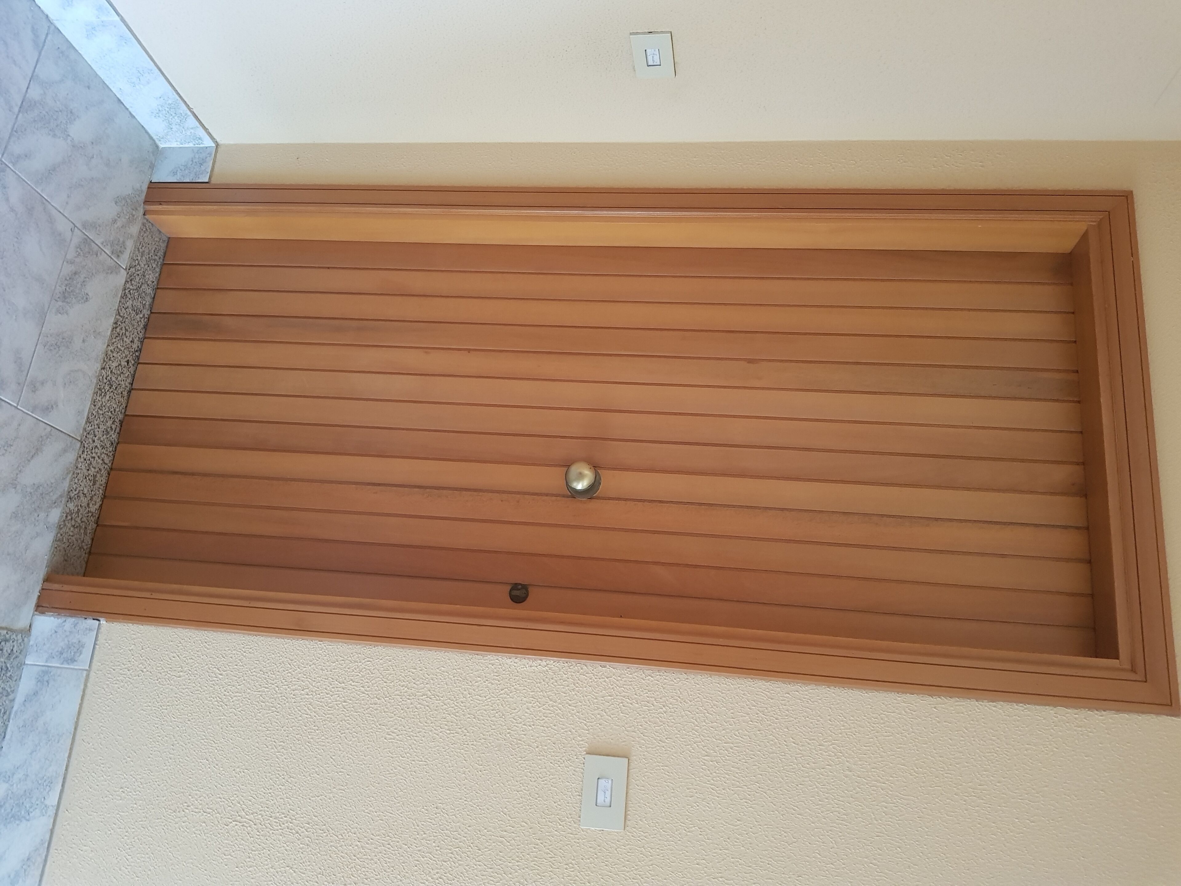 Eine Holzbalkendecke mit einer eingelassenen Vertiefung, einem Lichtschalter und einem Türrahmen.