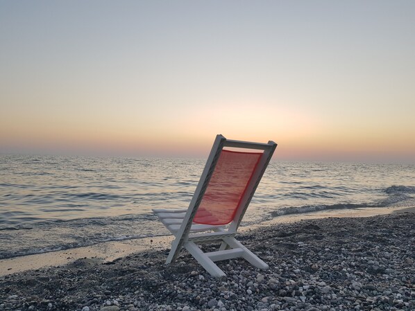 Una silla de playa en una costa rocosa, con vista al mar y un atardecer de fondo.