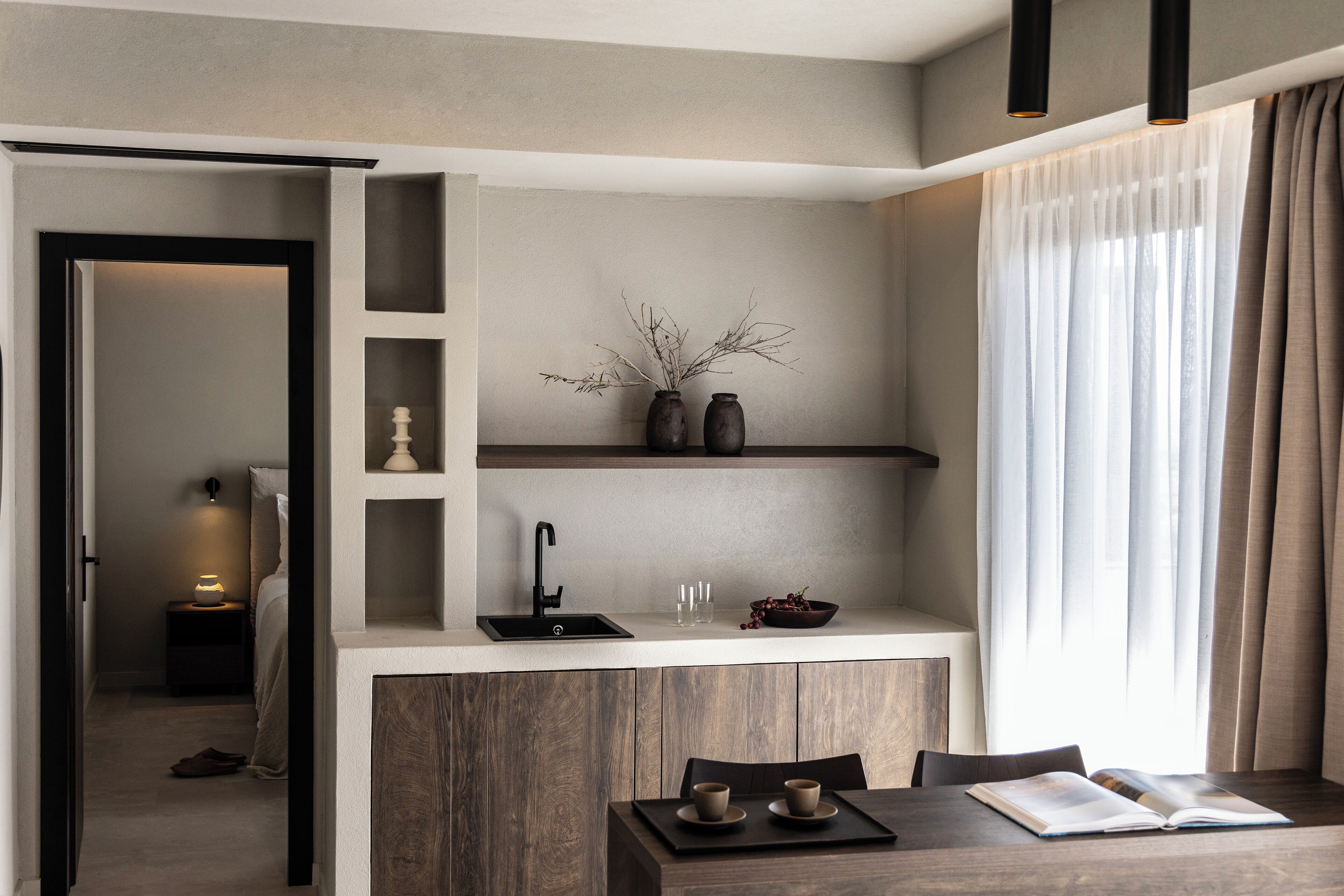 A modern kitchen with a built-in island, a dining area with a table and chairs, and a view of a bedroom through an open door.