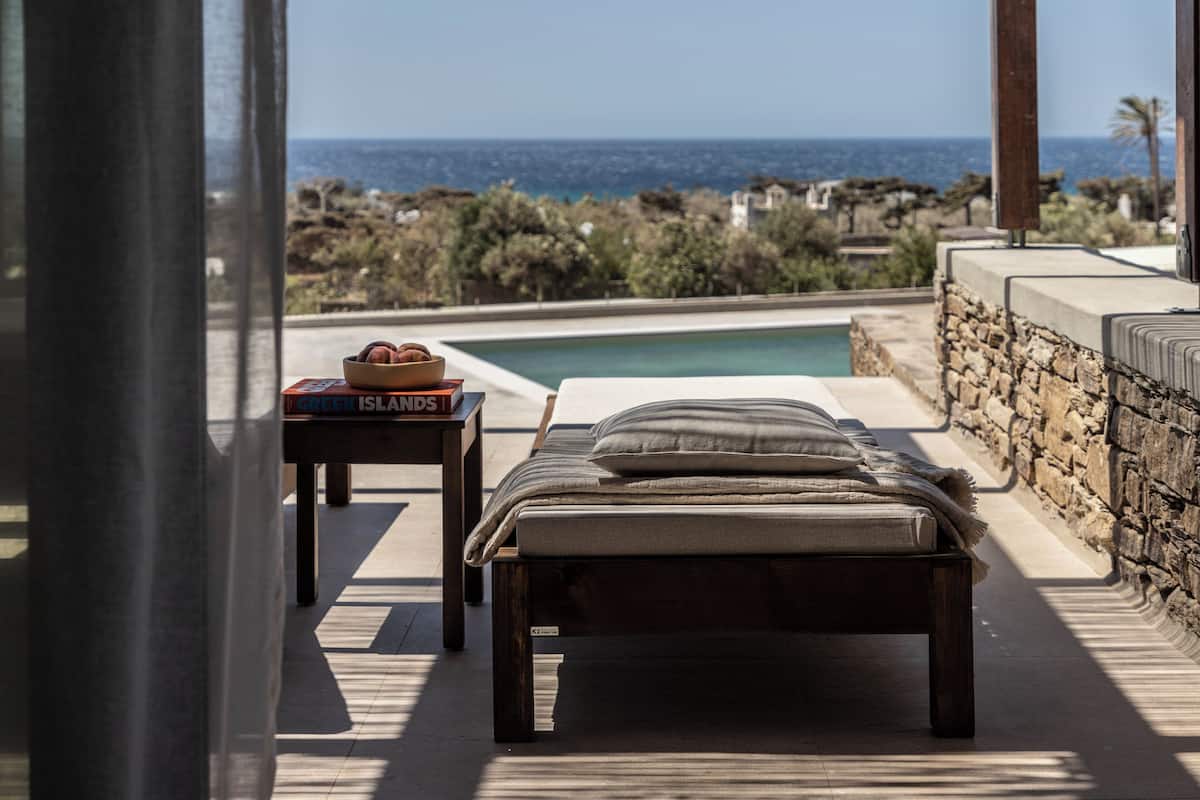 A bedroom with a view of the sea, a pool, and a stone wall.