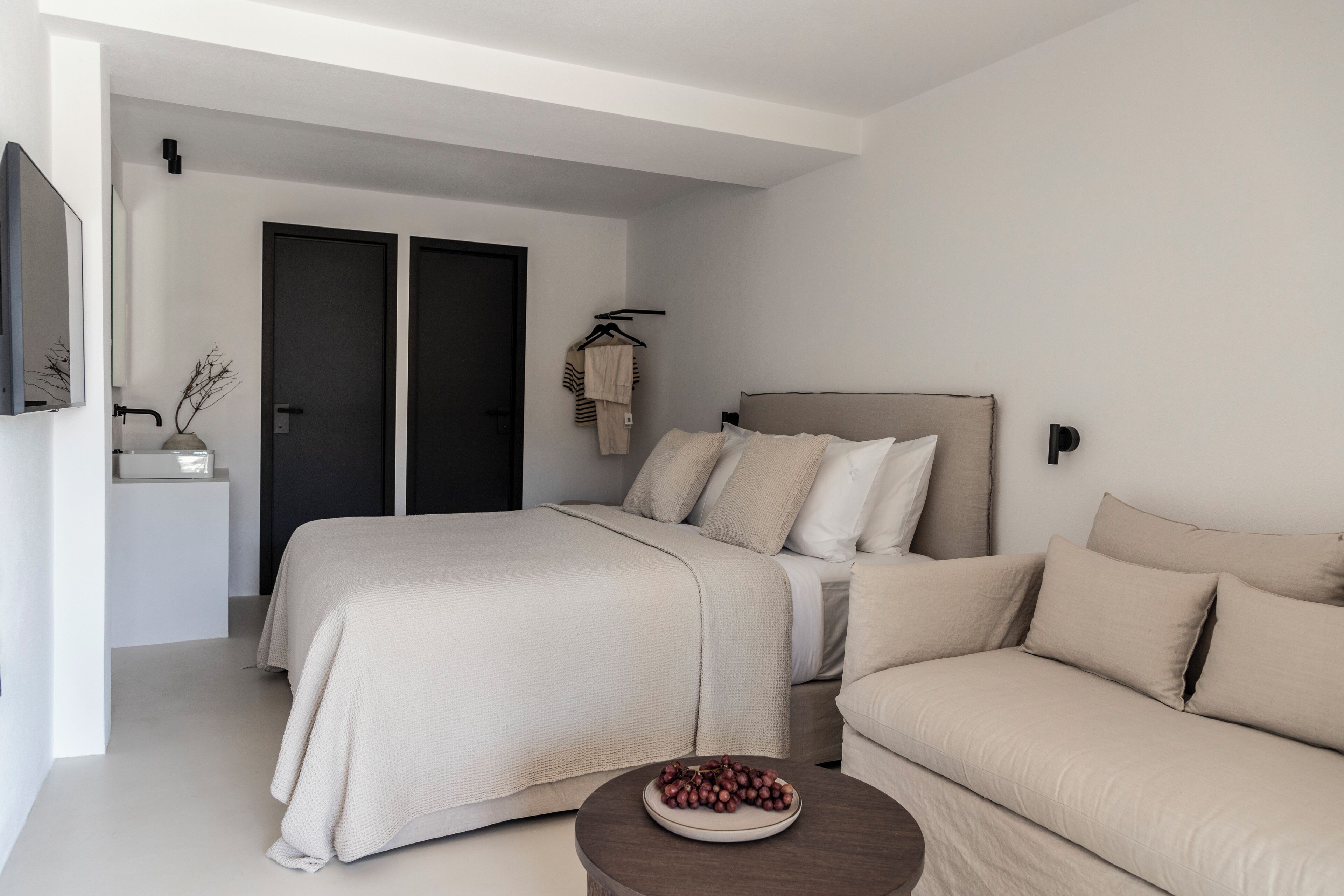 A modern bedroom with a bed, a sofa, a bedside table, and a wall-mounted TV.