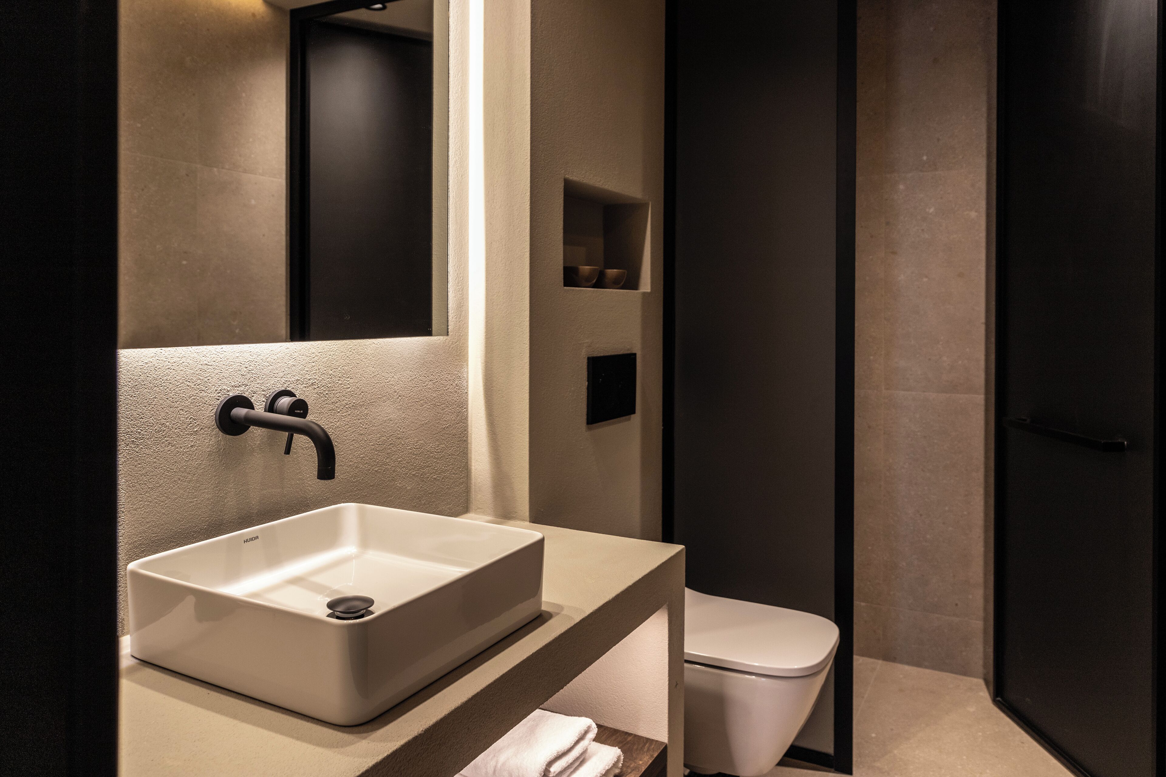 A modern bathroom with a large rectangular sink, a toilet, and a dark door.