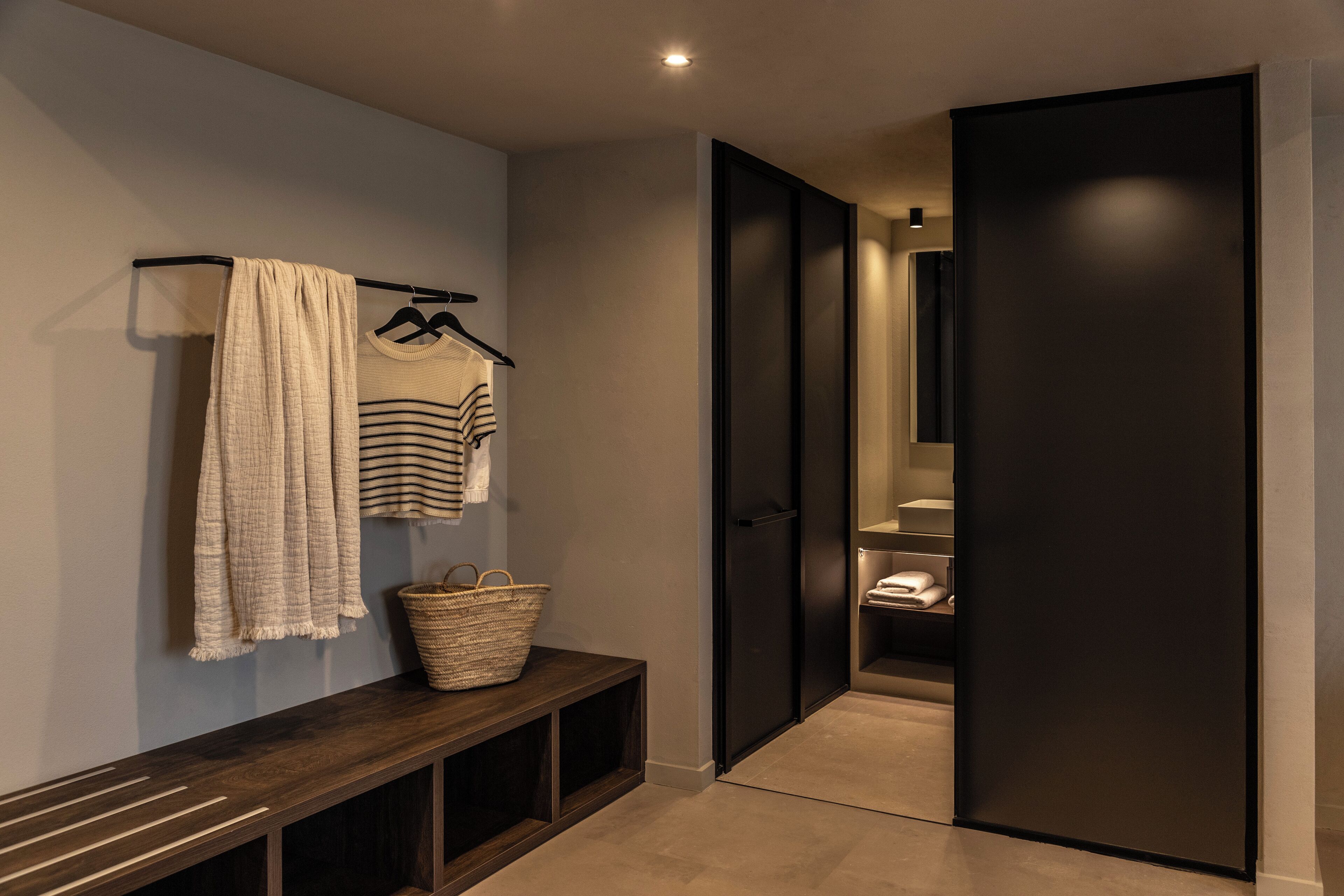 A hallway with a bench, a basket, and a clothing rack with towels and a striped shirt.