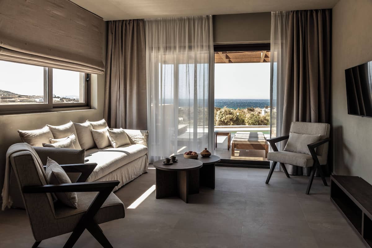 A modern living room with a sofa, armchairs, a coffee table, and a view of the sea.