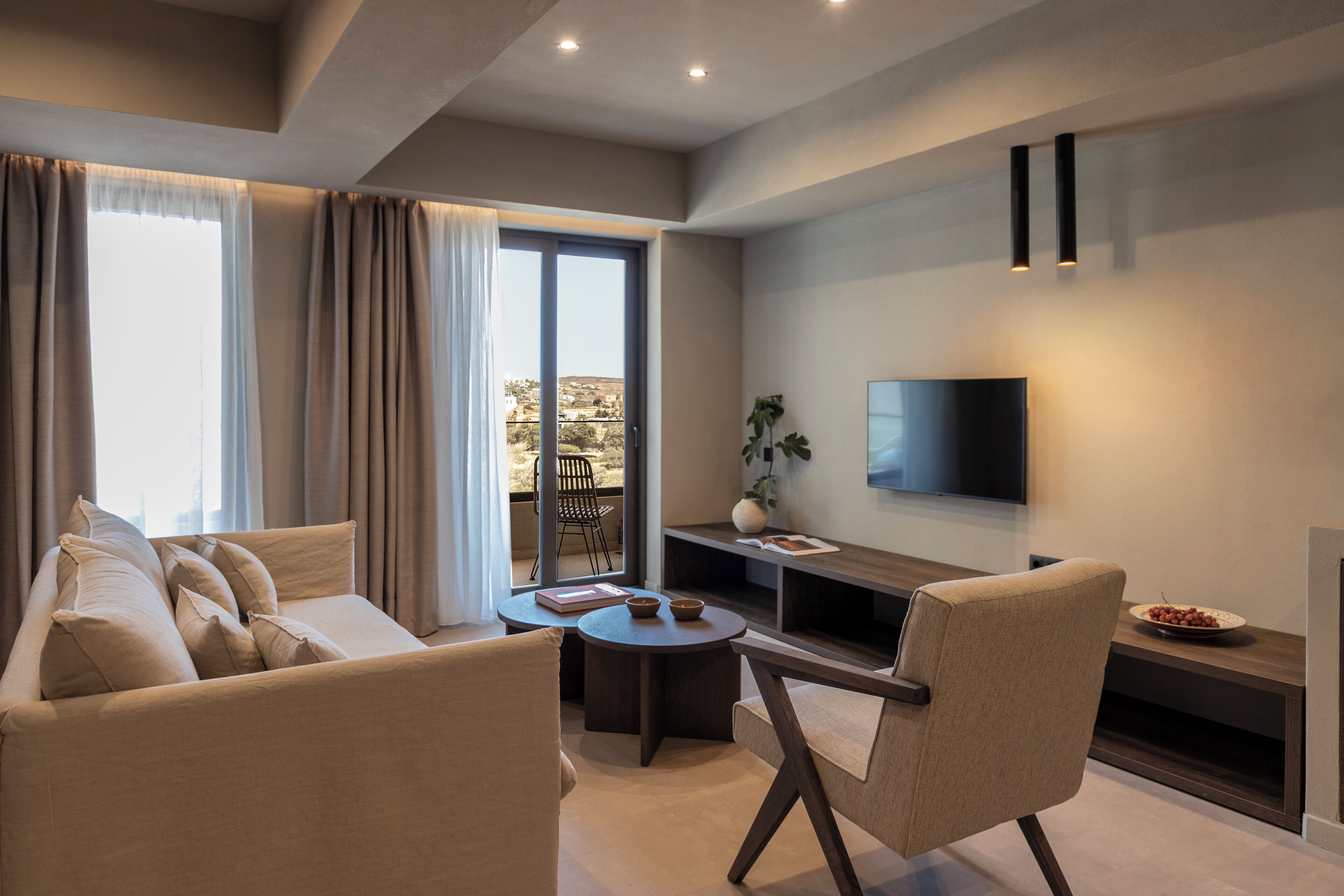 A modern living room with a sofa, armchair, coffee table, and a flat-screen TV mounted on the wall.