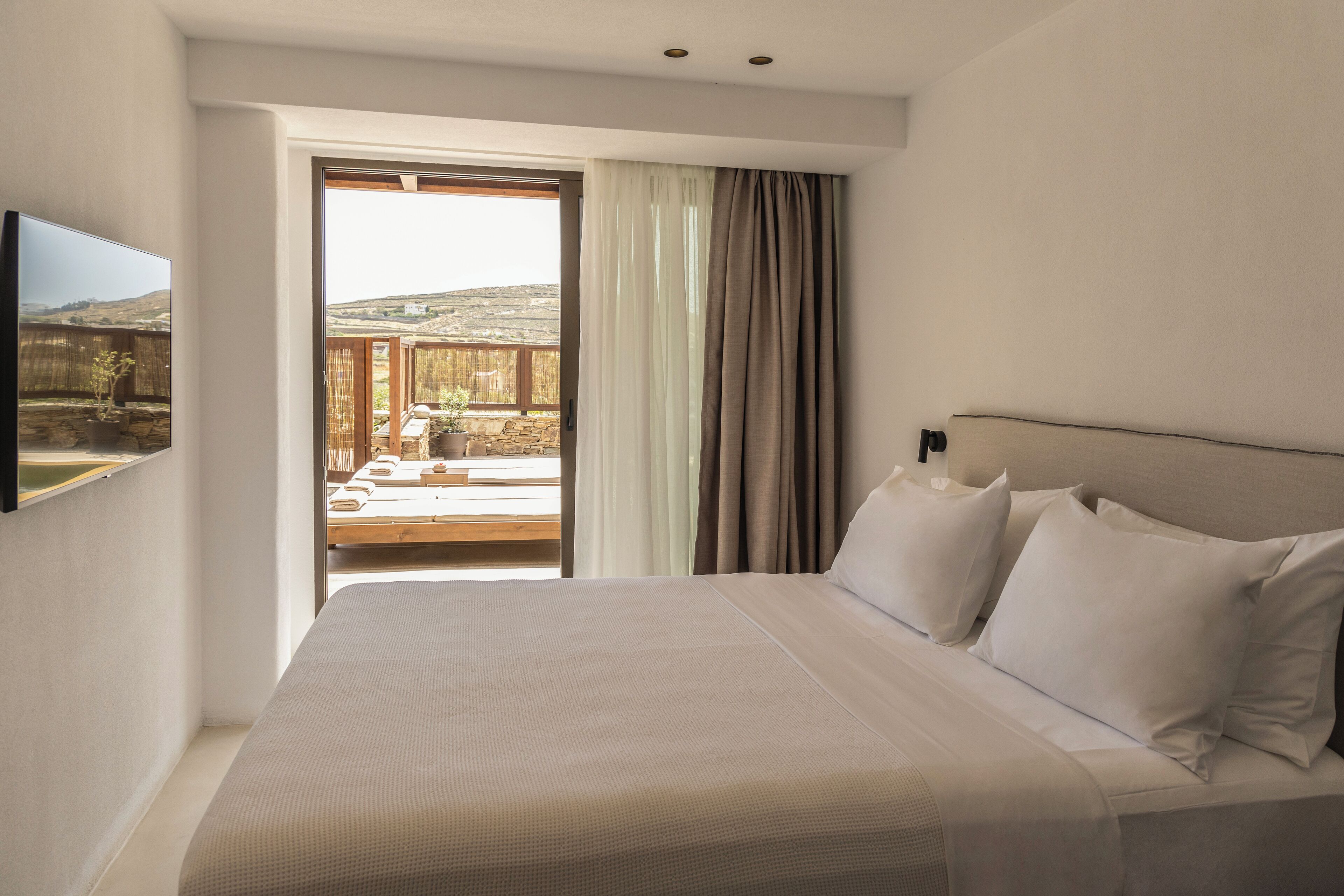 A bedroom with a large bed, a television on the wall, and a view of a balcony with a wooden fence.