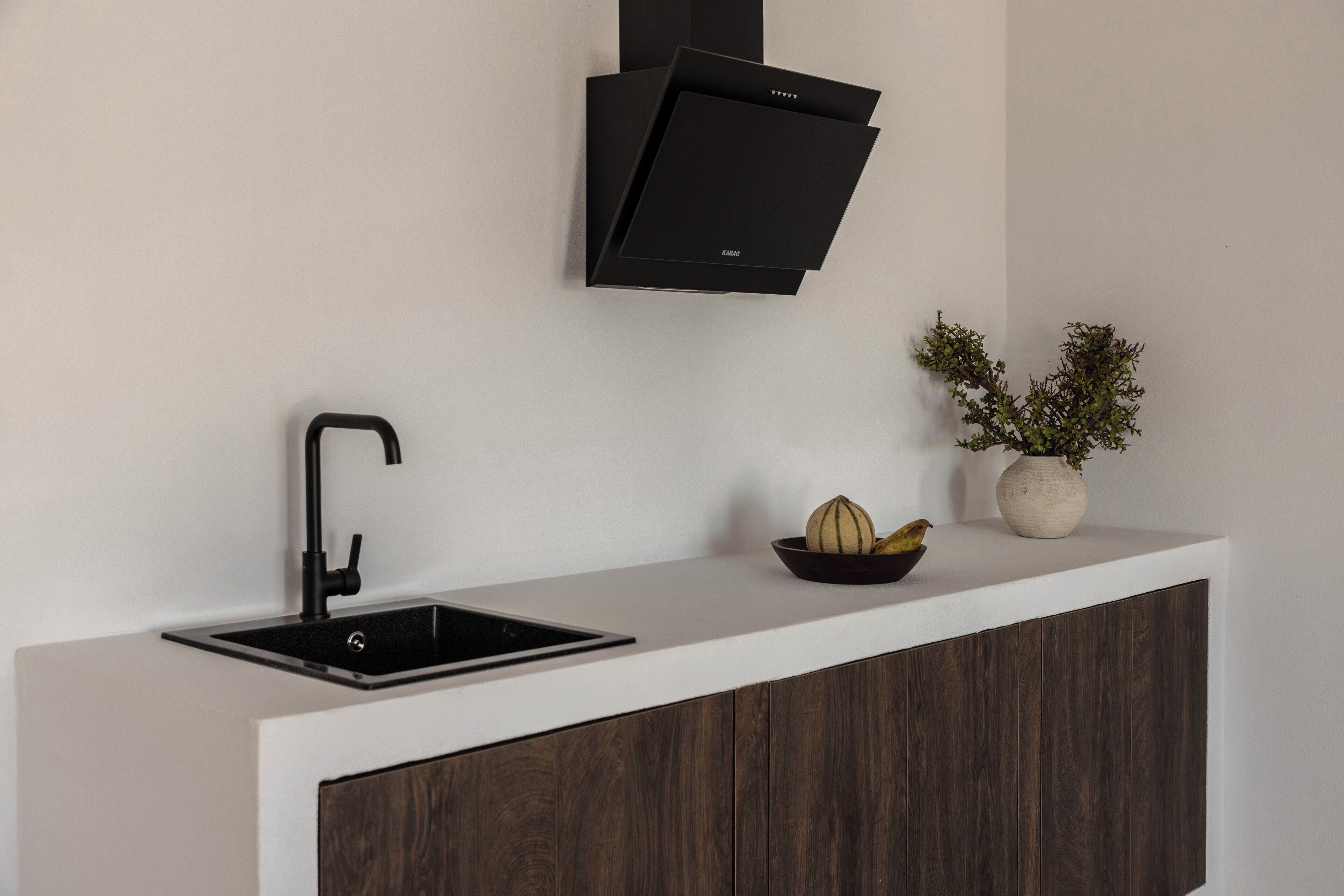 A modern kitchen with a black faucet, a built-in sink, a white countertop, and a dark wood cabinet.