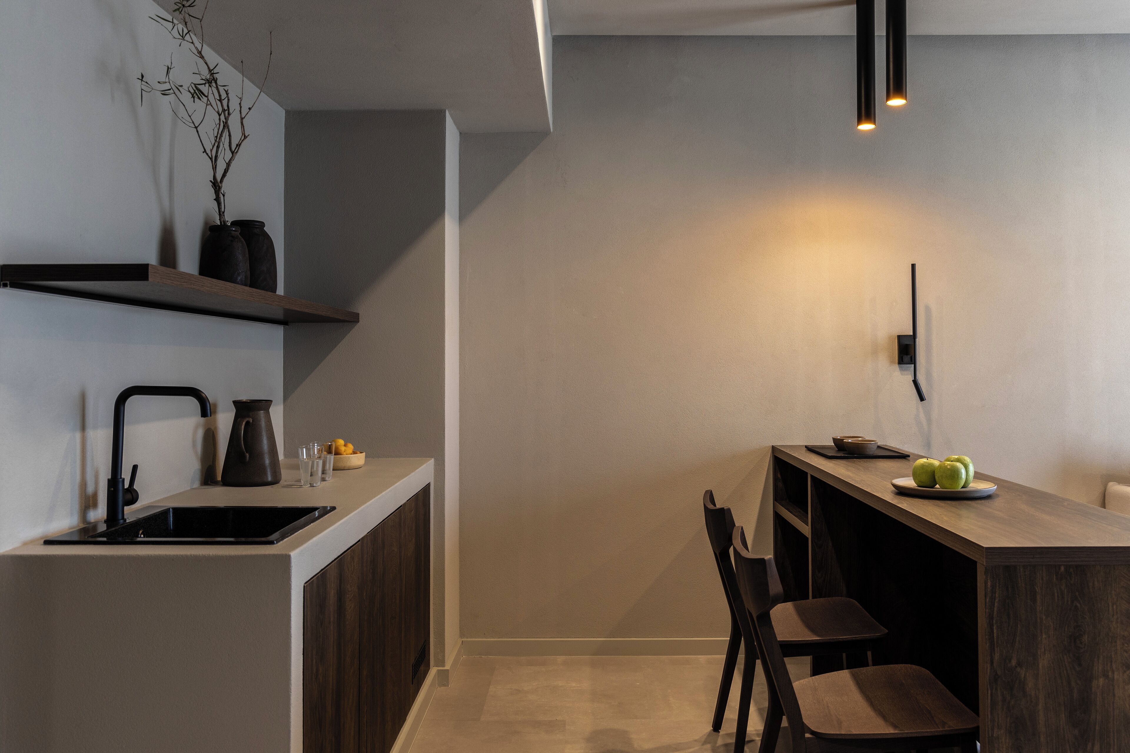 A modern kitchen with a built-in sink, dark wooden cabinets, a black countertop, and a dining area with a chair and a plate of apples.