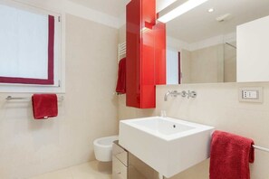A modern bathroom with a white sink, red towel, and a large mirror.