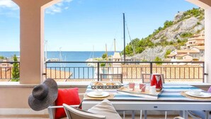 Ein Balkon mit Frühstückstisch, Blick auf eine Küstenlandschaft mit Gebäuden und Meer.