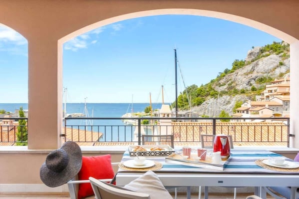 A balcony with a table set for breakfast, overlooking a coastal area with buildings and a view of the sea.