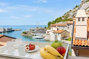 A tray with fruit and cups on a balcony overlooking a marina with boats and buildings.