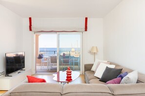 A living room with a TV, sofa, table, and a view through a sliding glass door to an outdoor area with chairs and a table.