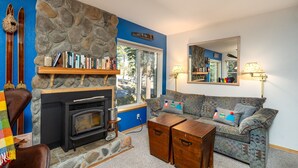 A cozy living room with a stone fireplace, a blue wall, and a large window.