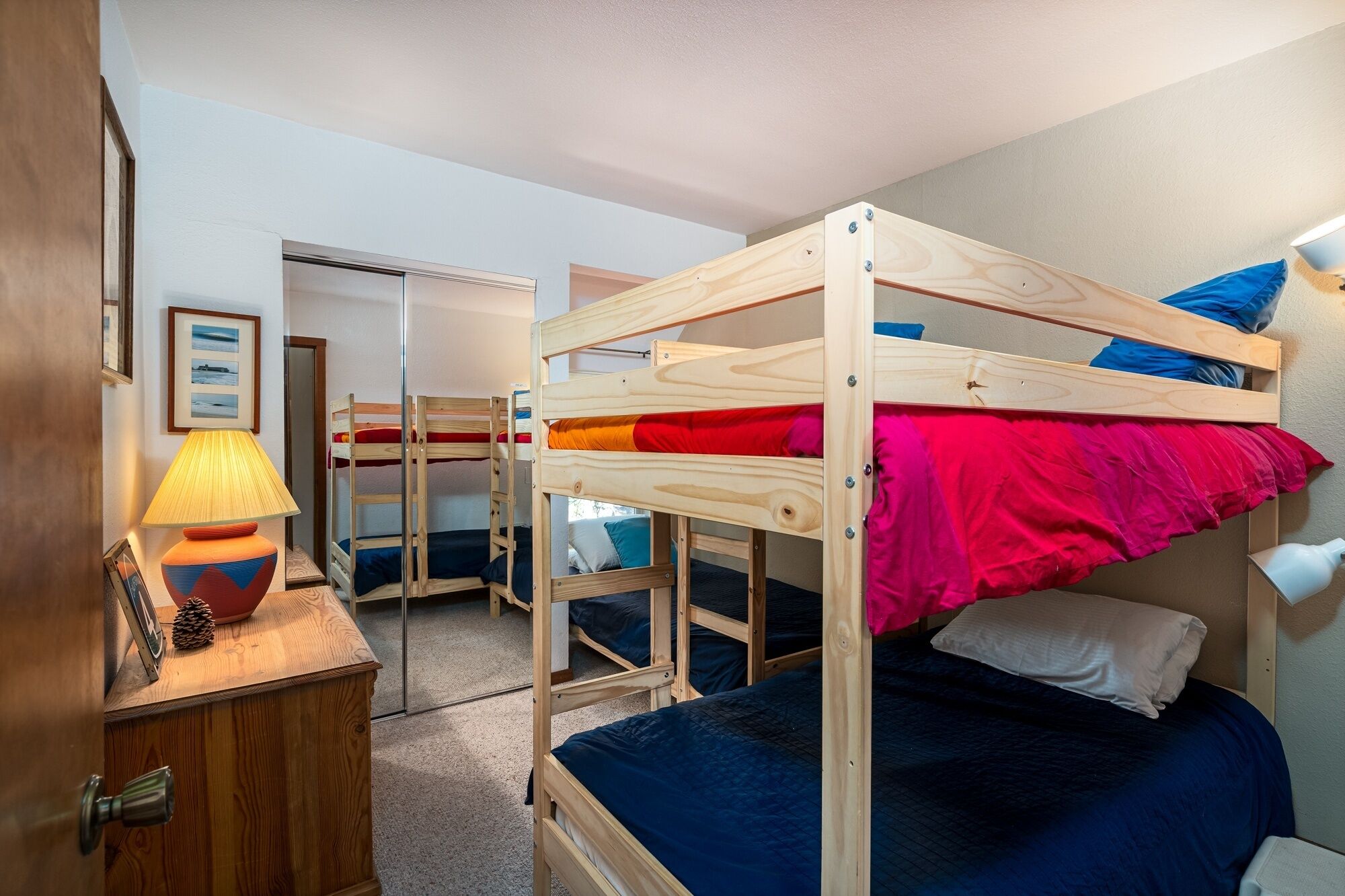 A bunk bed room with a wooden frame, a desk with a lamp, and a door.