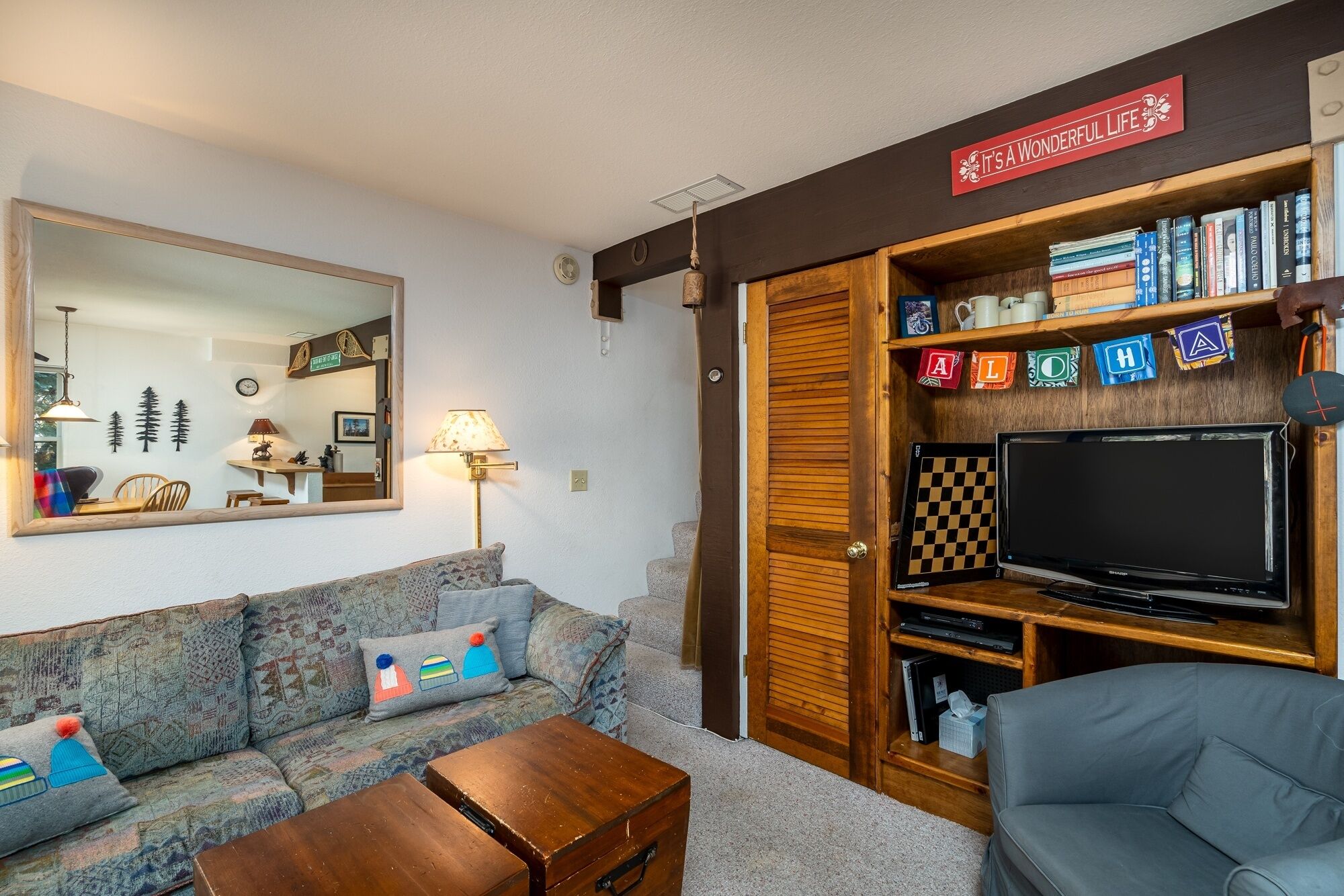 Un salón acogedor con un sofá, una mesa de centro, un televisor y una estantería llena de libros y objetos decorativos.