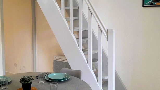 A dining area with a round table set for four, a potted plant, and a staircase with white railings. - Beachfront Villa with WiFi, Terrace & Parking - Sleeps 4 (Capbreton)