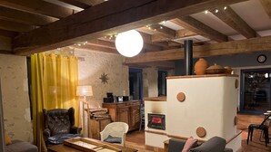 Ein rustikales Wohnzimmer mit sichtbaren Holzbalken, einem traditionellen Kaminofen und einer gemütlichen Sitzecke mit Sofa und Sesseln.