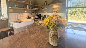 Eine Küche mit einer Marmarbeiteplatte, einem Spülbecken und einem Blumenstrauß. Über der Arbeitsfläche befinden sich Regale mit verschiedenen Küchenutensilien.