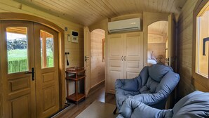 L'intérieur d'un chalet confortable, avec des murs en bois, une porte en bois, une petite table, un coin salon avec des coussins et un appareil de climatisation visible.