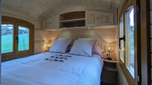 Une chambre à coucher dans un chalet en bois, avec un lit, deux lampes de chevet, une fenêtre et des placards intégrés.