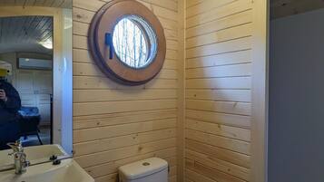 Een badkamer met houten wanden, een rond raam, een wastafel en een toilet.