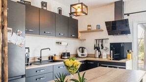 Une cuisine moderne avec des meubles de couleur sombre, un plan de travail en bois, une machine à café, une bouilloire et un porte-ustensiles suspendu.