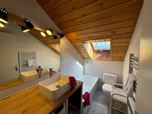 A modern bathroom with a wooden ceiling, a large mirror, a sink, a bathtub, and a toilet.