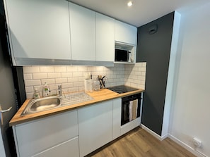 A modern kitchen with white cabinets, a wooden countertop, a stainless steel sink, and a microwave.