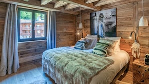 A cozy log cabin bedroom with a bed, a window with curtains, a painting, and a nightstand with a lamp. - Luxury Duplex in Val-d'Isère with Jacuzzi and Hammam (Val-d'Isère)